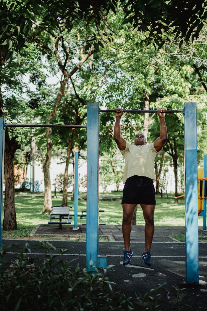 African American man doing pull-ups on outdoor exercise equipment in a sunny park setting.